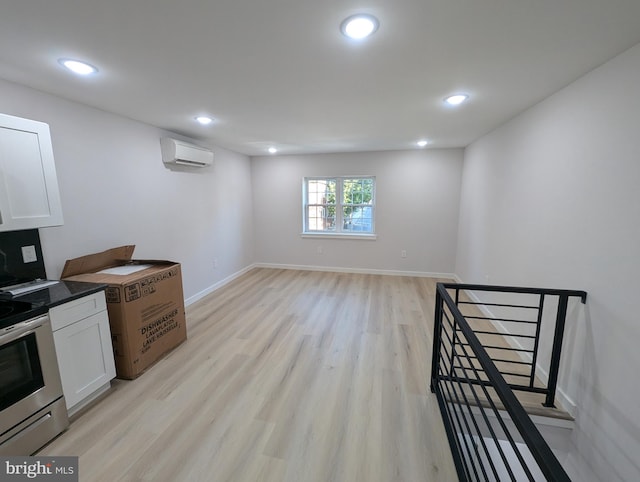 kitchen with light hardwood / wood-style flooring, white cabinets, a wall mounted AC, and stainless steel stove