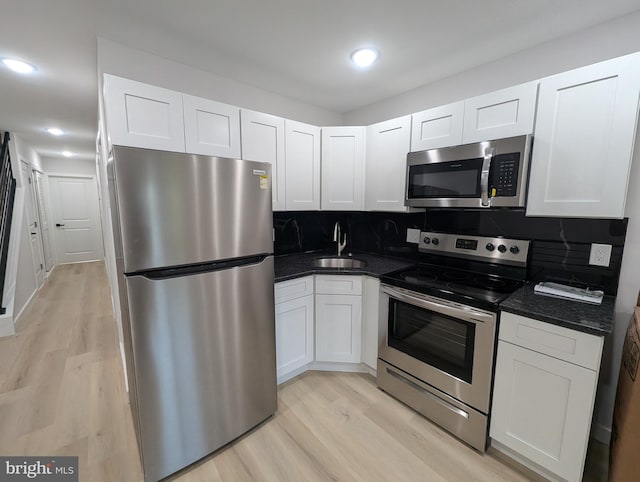 kitchen with appliances with stainless steel finishes, light hardwood / wood-style flooring, white cabinetry, and decorative backsplash