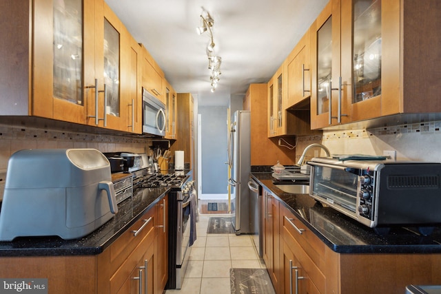 kitchen with appliances with stainless steel finishes, dark stone countertops, tasteful backsplash, light tile patterned floors, and sink