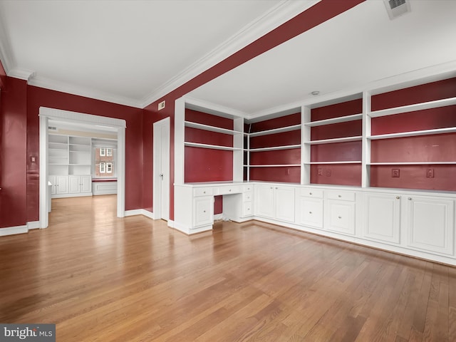 unfurnished living room with light wood finished floors, built in desk, visible vents, and ornamental molding