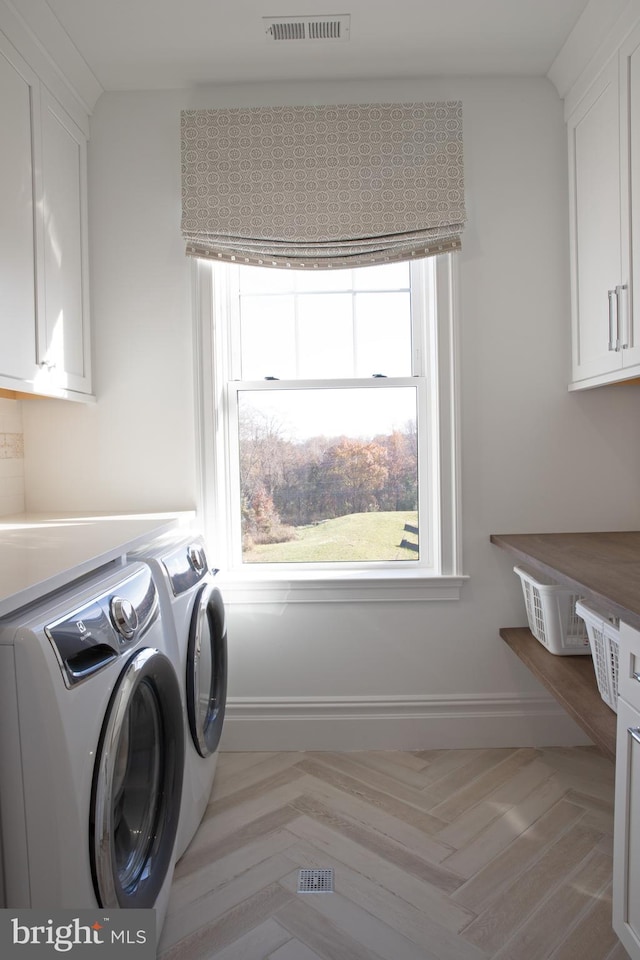 washroom featuring washing machine and clothes dryer, light parquet flooring, and cabinets