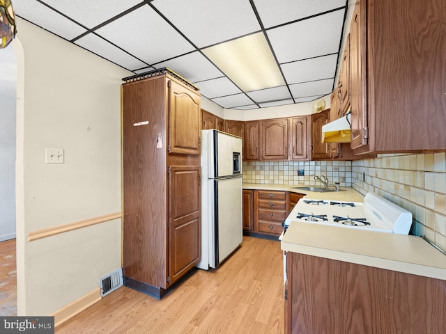 kitchen featuring decorative backsplash, light hardwood / wood-style flooring, a drop ceiling, sink, and white appliances