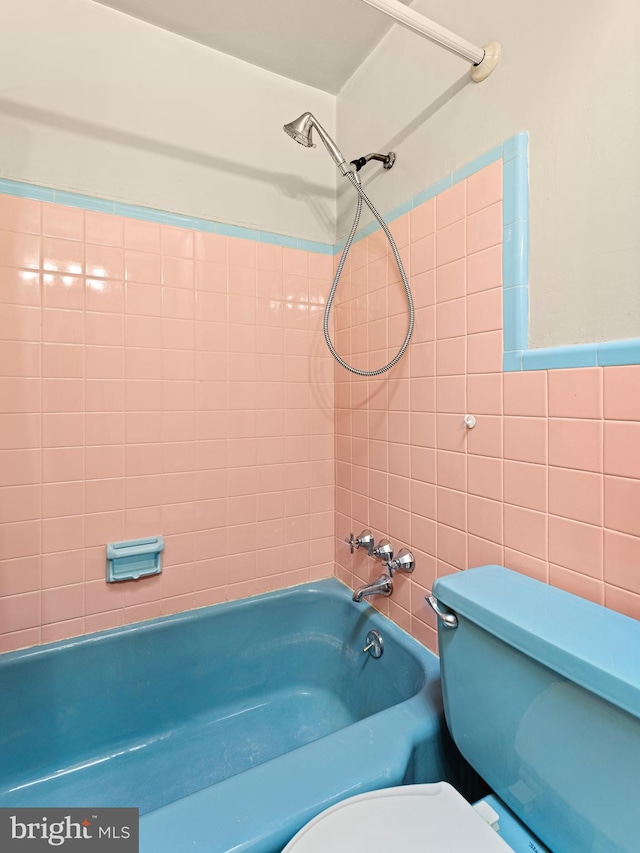 bathroom with toilet, tiled shower / bath combo, and tile walls