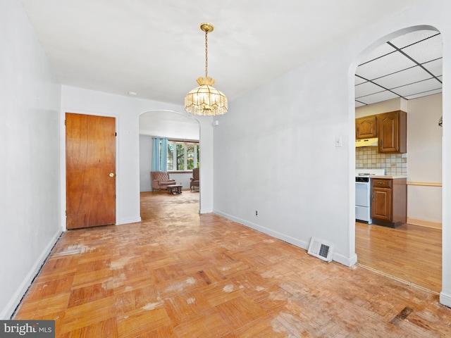 unfurnished dining area featuring light parquet flooring, a drop ceiling, and an inviting chandelier