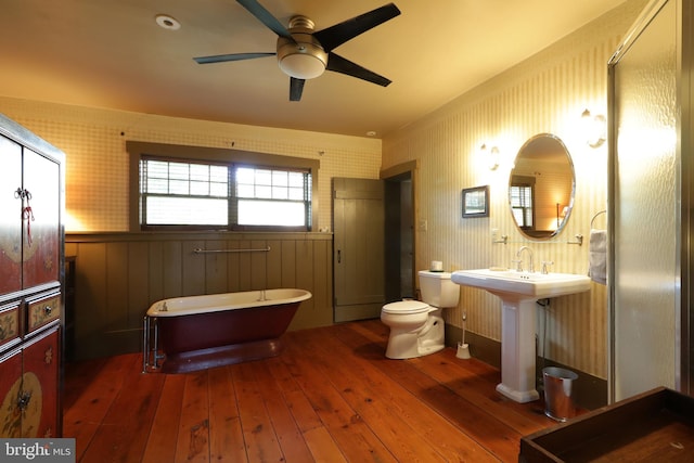 bathroom with wood-type flooring, a bath, wooden walls, ceiling fan, and toilet