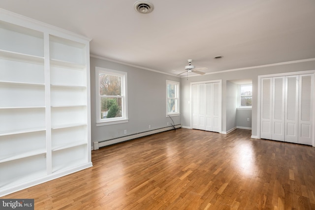 unfurnished bedroom featuring a baseboard heating unit, crown molding, dark hardwood / wood-style floors, and multiple closets