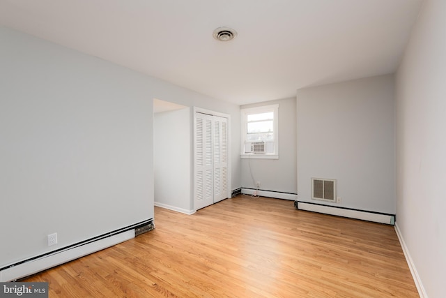 unfurnished bedroom featuring a closet, a baseboard heating unit, and light hardwood / wood-style flooring