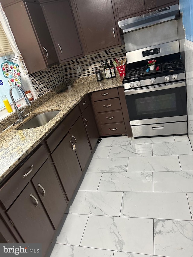 kitchen featuring light stone countertops, sink, dark brown cabinetry, gas range, and decorative backsplash