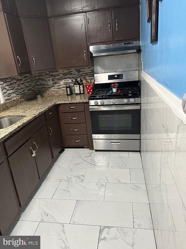 kitchen with sink, backsplash, dark brown cabinetry, stainless steel gas range oven, and dark stone countertops