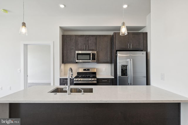 kitchen featuring tasteful backsplash, hanging light fixtures, appliances with stainless steel finishes, light stone countertops, and sink