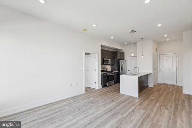 kitchen with sink, stainless steel appliances, dark brown cabinetry, pendant lighting, and light hardwood / wood-style flooring