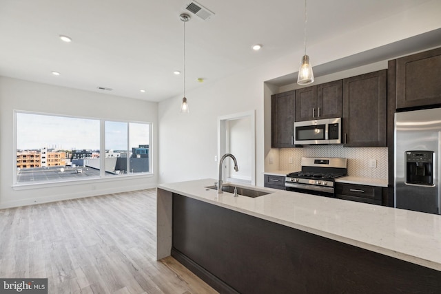 kitchen with sink, hanging light fixtures, light hardwood / wood-style floors, stainless steel appliances, and light stone counters