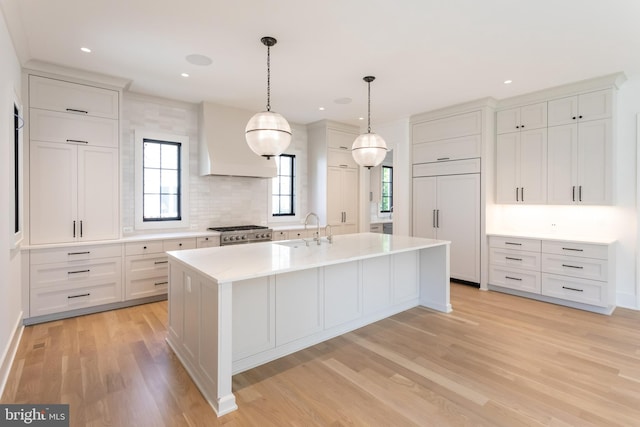 kitchen featuring a center island with sink, paneled built in fridge, white cabinets, stainless steel range, and light hardwood / wood-style flooring