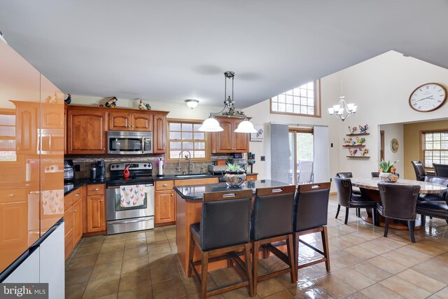 kitchen with tasteful backsplash, sink, hanging light fixtures, a kitchen island, and appliances with stainless steel finishes