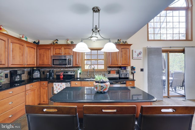 kitchen featuring backsplash, decorative light fixtures, appliances with stainless steel finishes, and a kitchen island