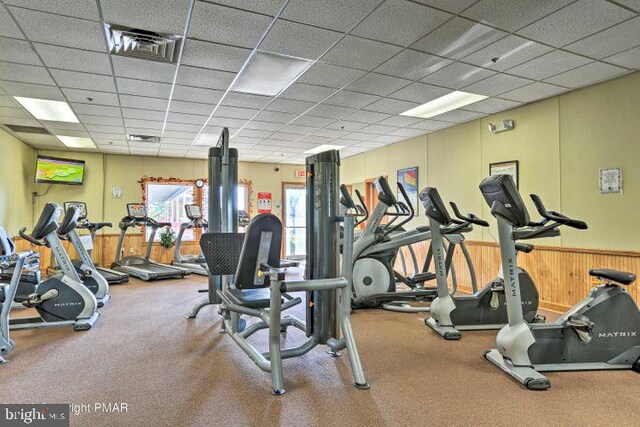 exercise room featuring wooden walls and a paneled ceiling