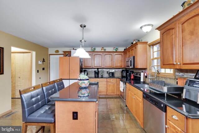 kitchen featuring pendant lighting, stainless steel appliances, a center island, a kitchen bar, and decorative backsplash