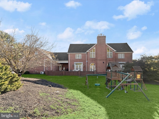 rear view of property featuring brick siding, a lawn, a chimney, and a playground