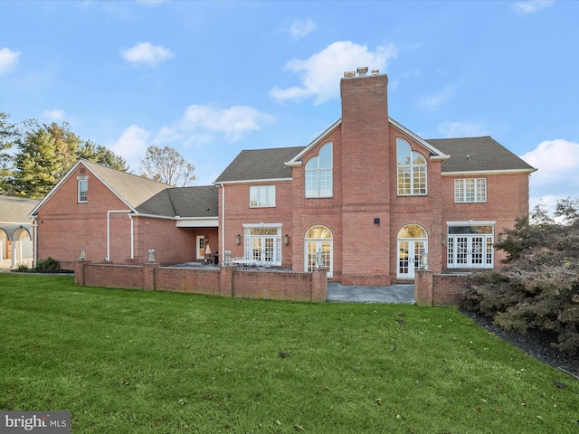 rear view of property with a patio, french doors, a yard, brick siding, and a chimney