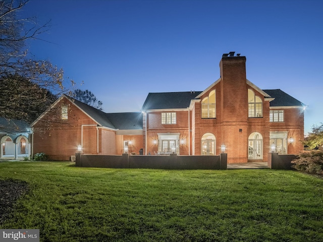 rear view of house featuring brick siding, french doors, a chimney, and a yard