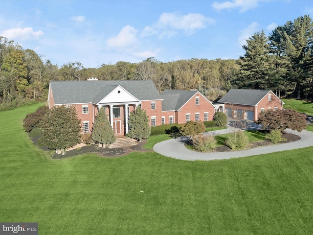 neoclassical home featuring a wooded view, entry steps, and a front yard