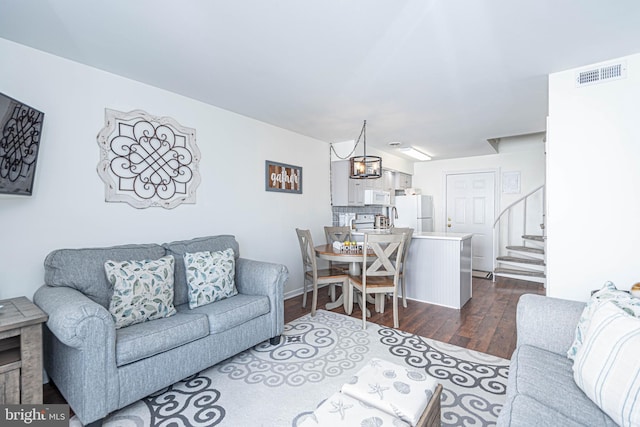 living room featuring a notable chandelier, visible vents, stairs, and dark wood finished floors