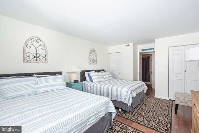 bedroom with visible vents, baseboards, multiple closets, and wood finished floors