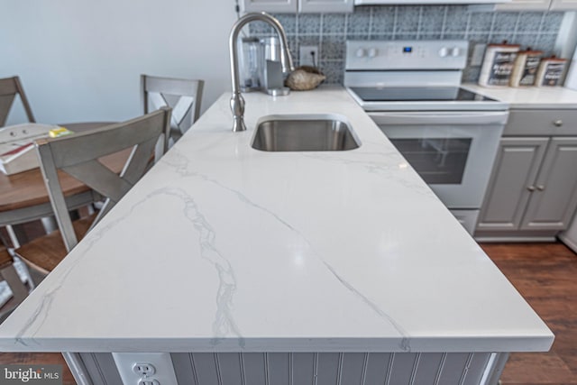 kitchen featuring electric range, sink, gray cabinets, a kitchen island with sink, and a breakfast bar