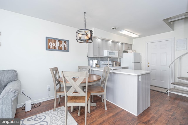 kitchen with kitchen peninsula, dark hardwood / wood-style flooring, white appliances, and a notable chandelier