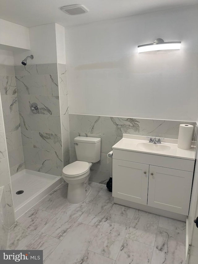 bathroom with tile walls, vanity, tiled shower, and toilet