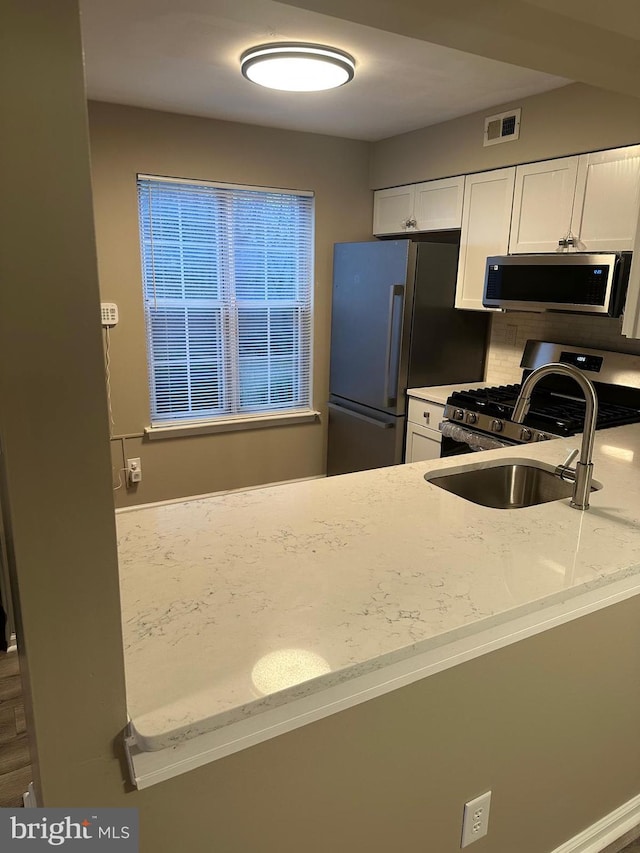 kitchen featuring appliances with stainless steel finishes, sink, light stone countertops, and white cabinets