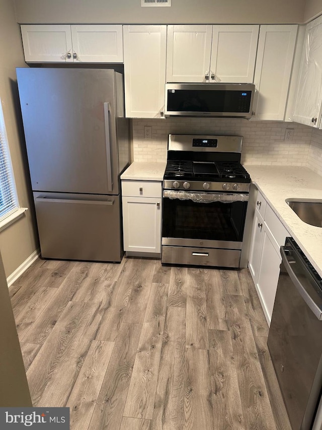 kitchen with white cabinets, light hardwood / wood-style flooring, stainless steel appliances, and tasteful backsplash