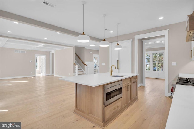 kitchen with beam ceiling, sink, coffered ceiling, an island with sink, and decorative light fixtures