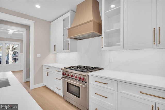 kitchen featuring white cabinetry, designer range, light hardwood / wood-style floors, and custom range hood