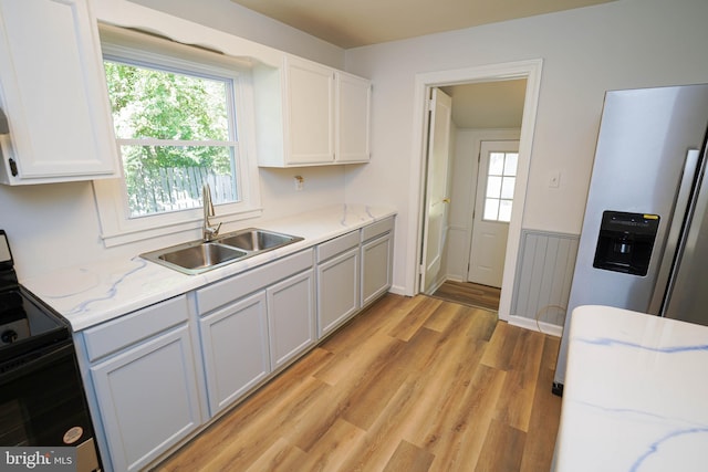 kitchen with white cabinetry, light wood-type flooring, light stone countertops, sink, and black range with electric stovetop