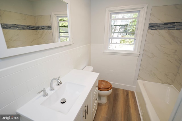 full bathroom with toilet, tile walls, hardwood / wood-style floors, tiled shower / bath combo, and vanity