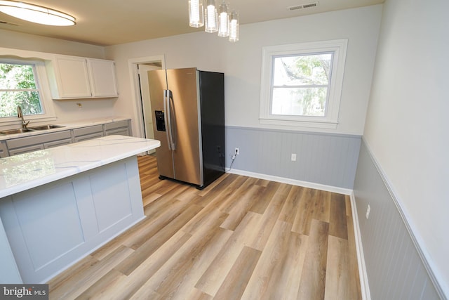 kitchen featuring stainless steel fridge with ice dispenser, plenty of natural light, pendant lighting, sink, and white cabinets