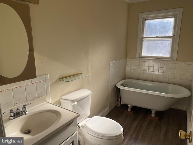 bathroom featuring a tub to relax in, toilet, wood-type flooring, tile walls, and vanity