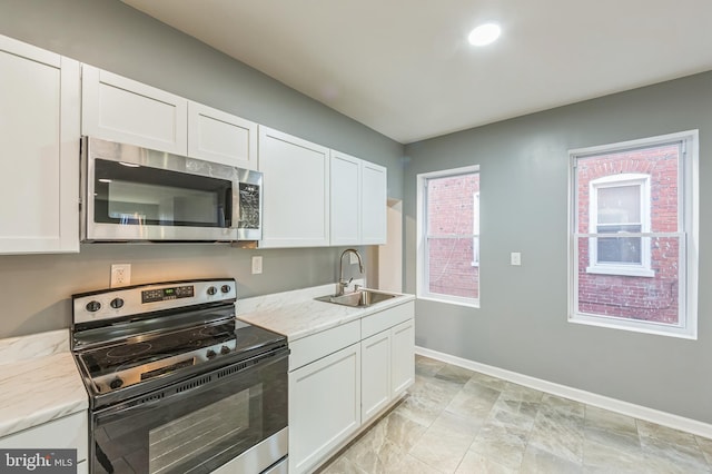 kitchen with sink, white cabinets, light stone counters, and stainless steel appliances