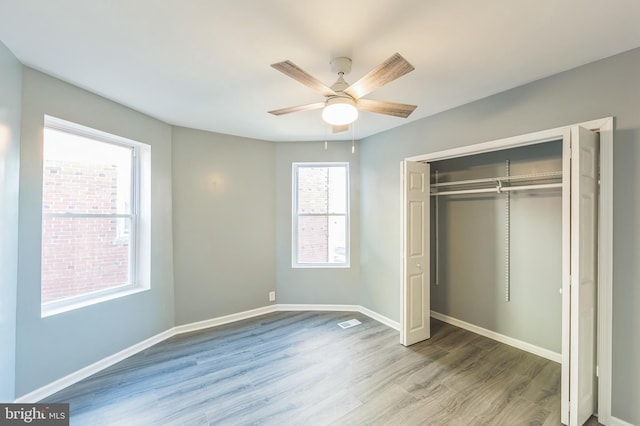 unfurnished bedroom with multiple windows, a closet, wood-type flooring, and ceiling fan