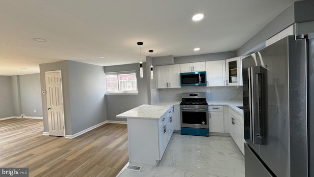 kitchen with white cabinets, kitchen peninsula, tasteful backsplash, appliances with stainless steel finishes, and light stone countertops