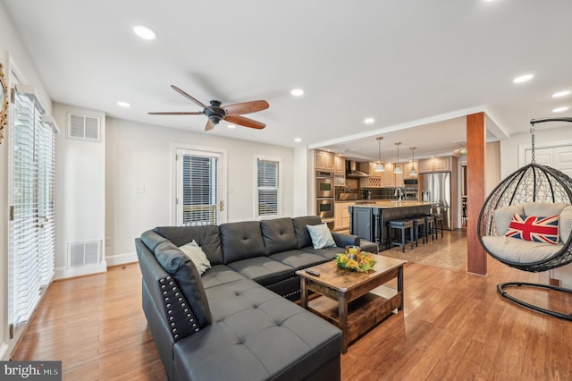 living room with ceiling fan, sink, and light wood-type flooring