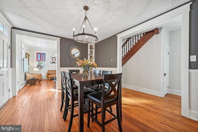 dining space with wood-type flooring, a baseboard heating unit, and a notable chandelier