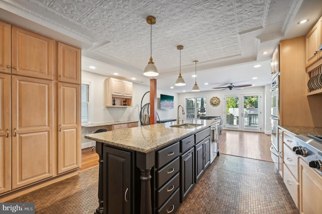 kitchen with ceiling fan, sink, dark wood-type flooring, light stone counters, and a center island with sink