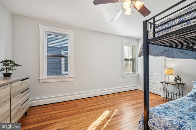 bedroom with ceiling fan, wood-type flooring, and a baseboard heating unit