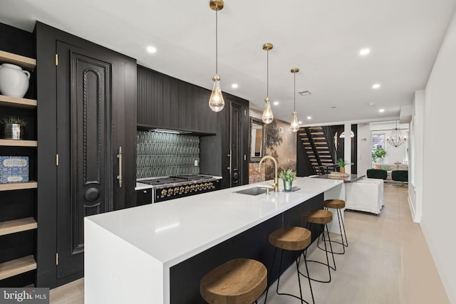 kitchen with sink, stainless steel gas cooktop, decorative light fixtures, a breakfast bar, and a kitchen island with sink