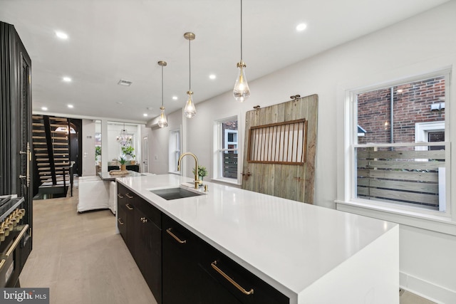 kitchen featuring a large island with sink, sink, hanging light fixtures, and light hardwood / wood-style floors