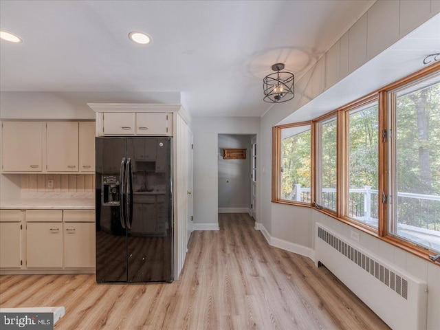 kitchen featuring white cabinets, black fridge, radiator, pendant lighting, and light hardwood / wood-style floors