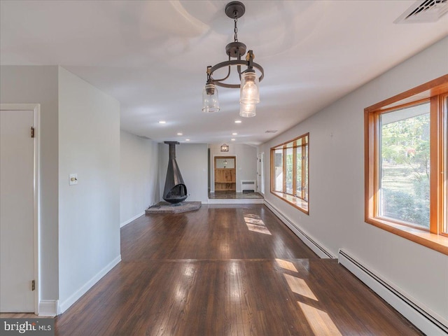 unfurnished living room featuring a wood stove, baseboard heating, and dark hardwood / wood-style flooring