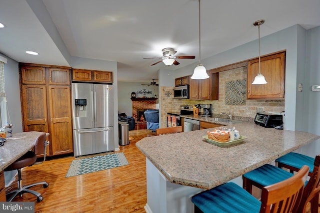 kitchen with light wood-type flooring, pendant lighting, a breakfast bar area, stainless steel appliances, and kitchen peninsula